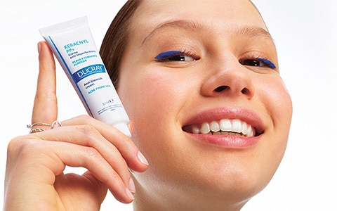 Jeune femme souriante tenant un produit Keracnyl de Ducray