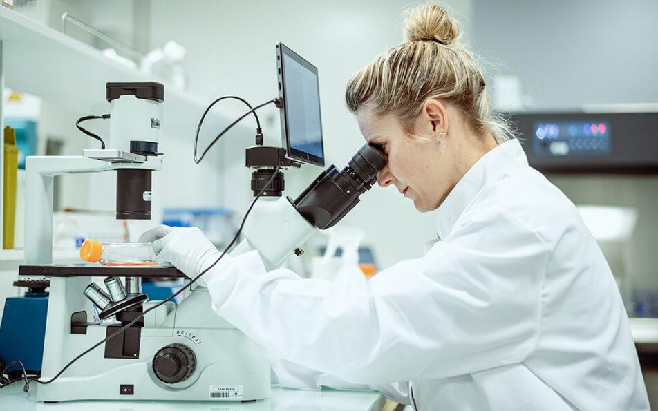 Une chercheuse en blouse blanche utilisant un microscope dans un laboratoire moderne, concentrée sur ses observations.